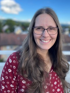 Friendly, smiling young woman with brown eyes, glasses and long brown hair.
