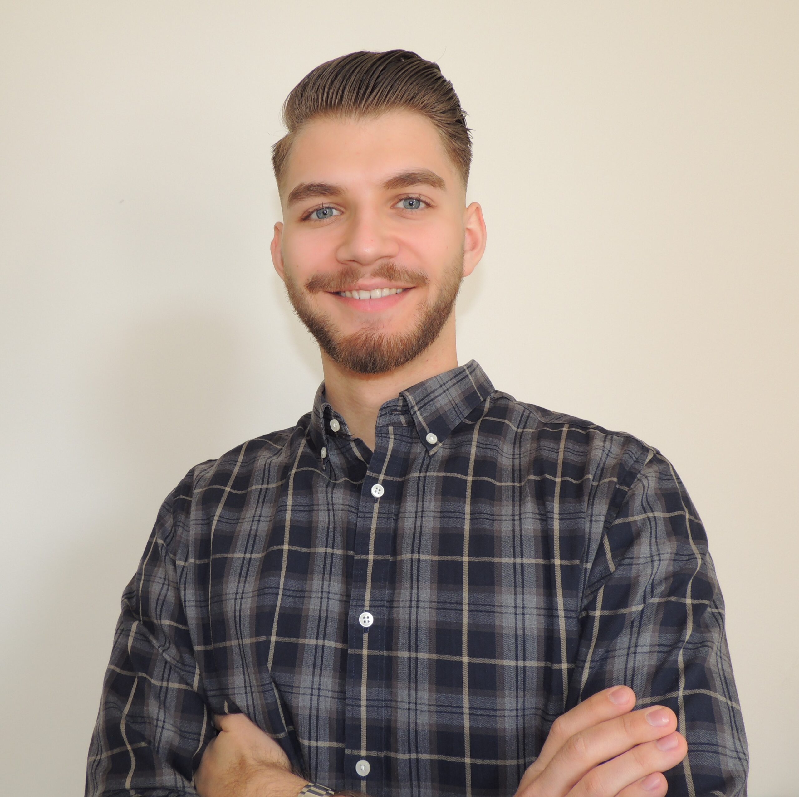 A friendly, smiling young man with blue eyes, a full beard and short brown hair.